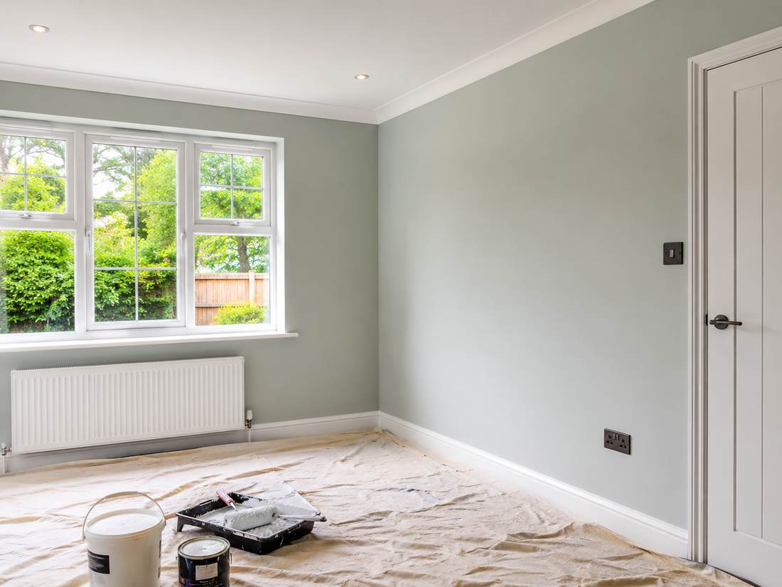Empty bedroom freshly painted in soft sage green, dust sheets and paint tray on the floor mid-decoration